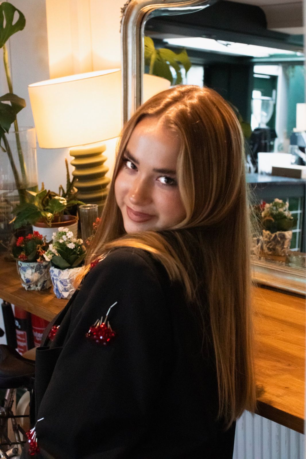 Model looking back over her shoulder and smiling, a lamp and flowers behind her