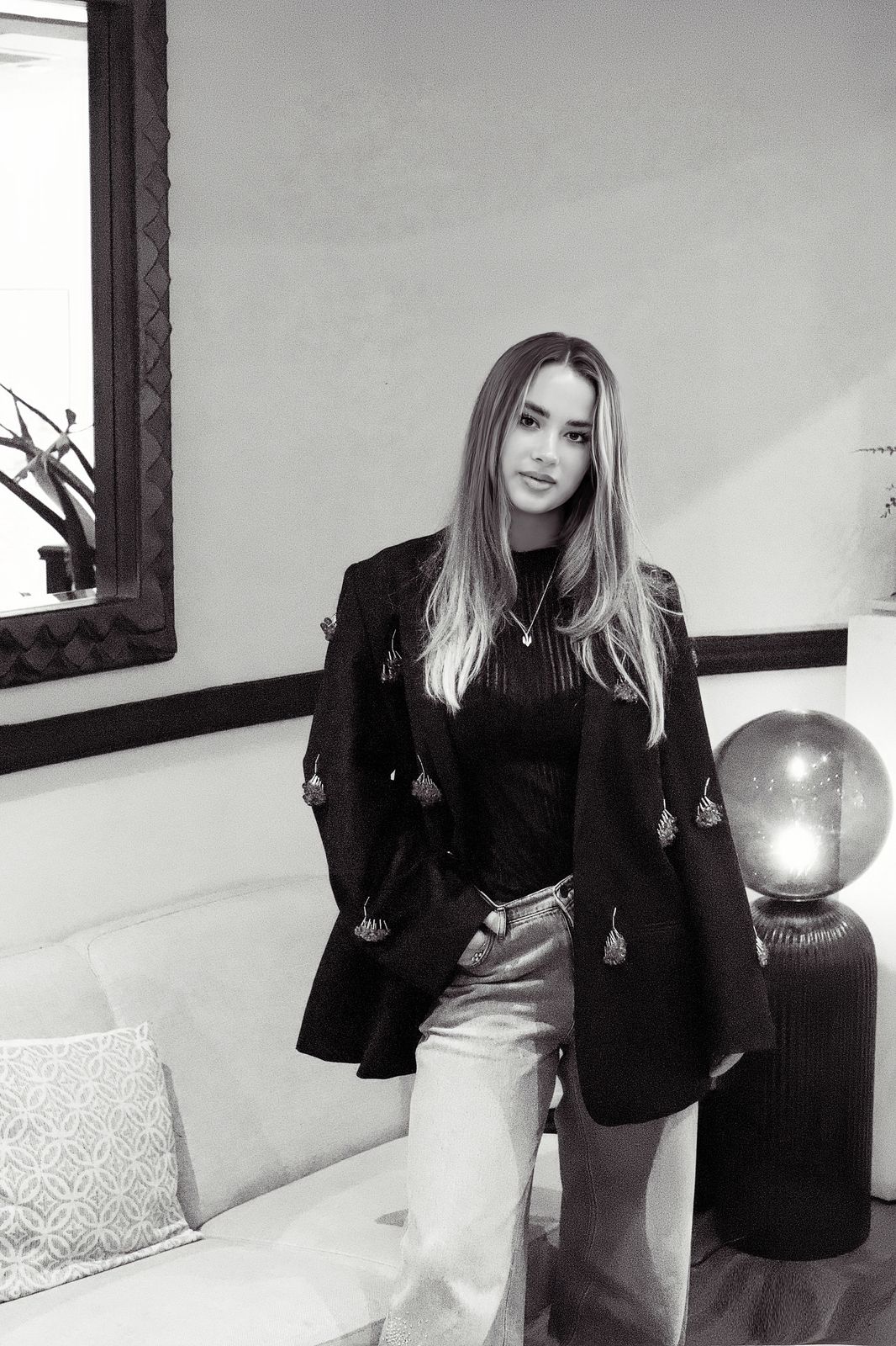 Black and white portrait of the model standing by a sofa and a glowing globe lamp