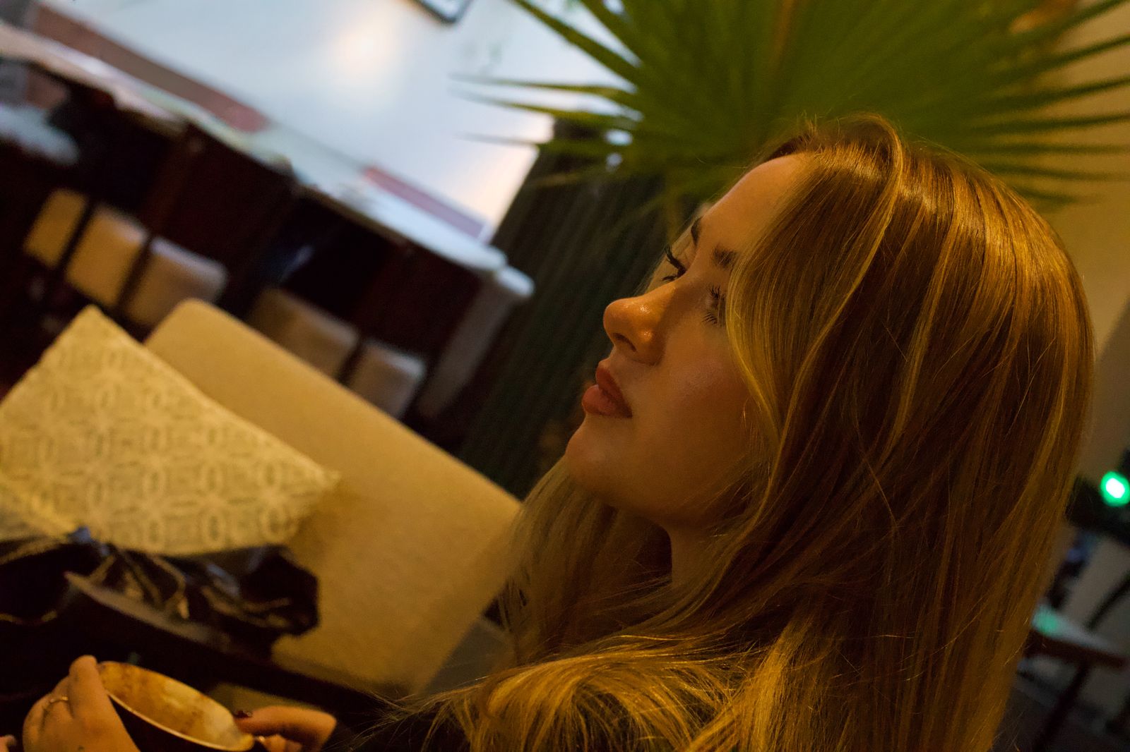Tilted close profile of the model holding a coffee cup, a palm behind her